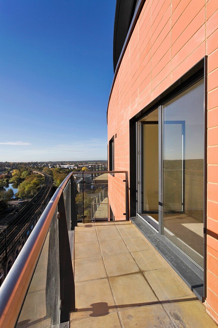 Balcony with stone tiles in front of a modern home with a bank of windows and a view of the surrounding area