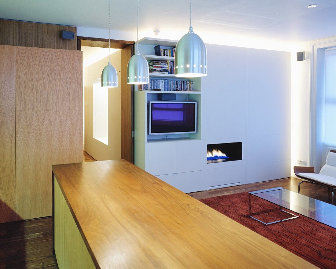 A wooden kitchen counter with a modern, stainless steel pendent lamp in an open-plan living room