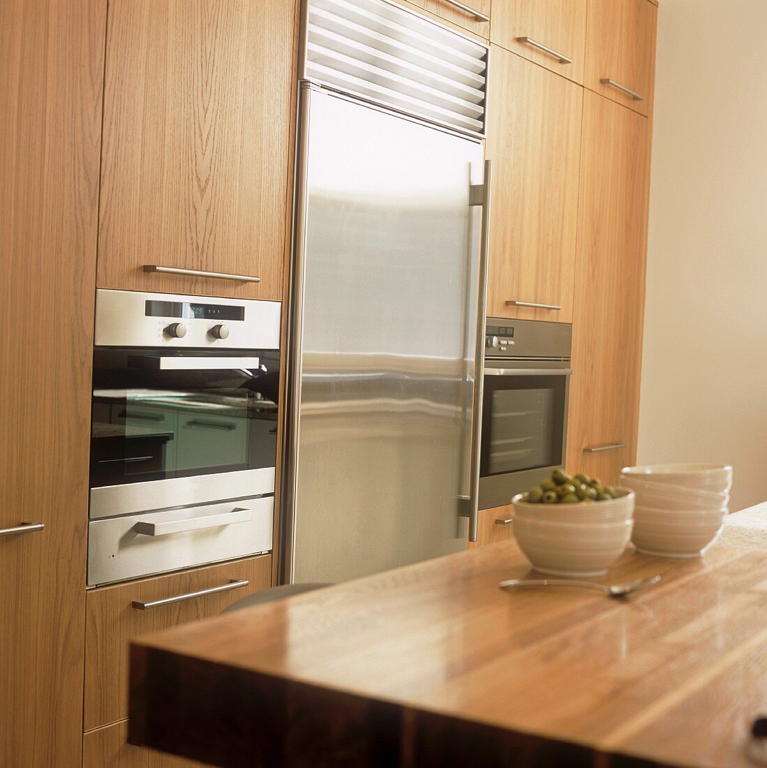 A stack of bowls on a wooden work surface in a kitchen with fitted cupboards and appliances