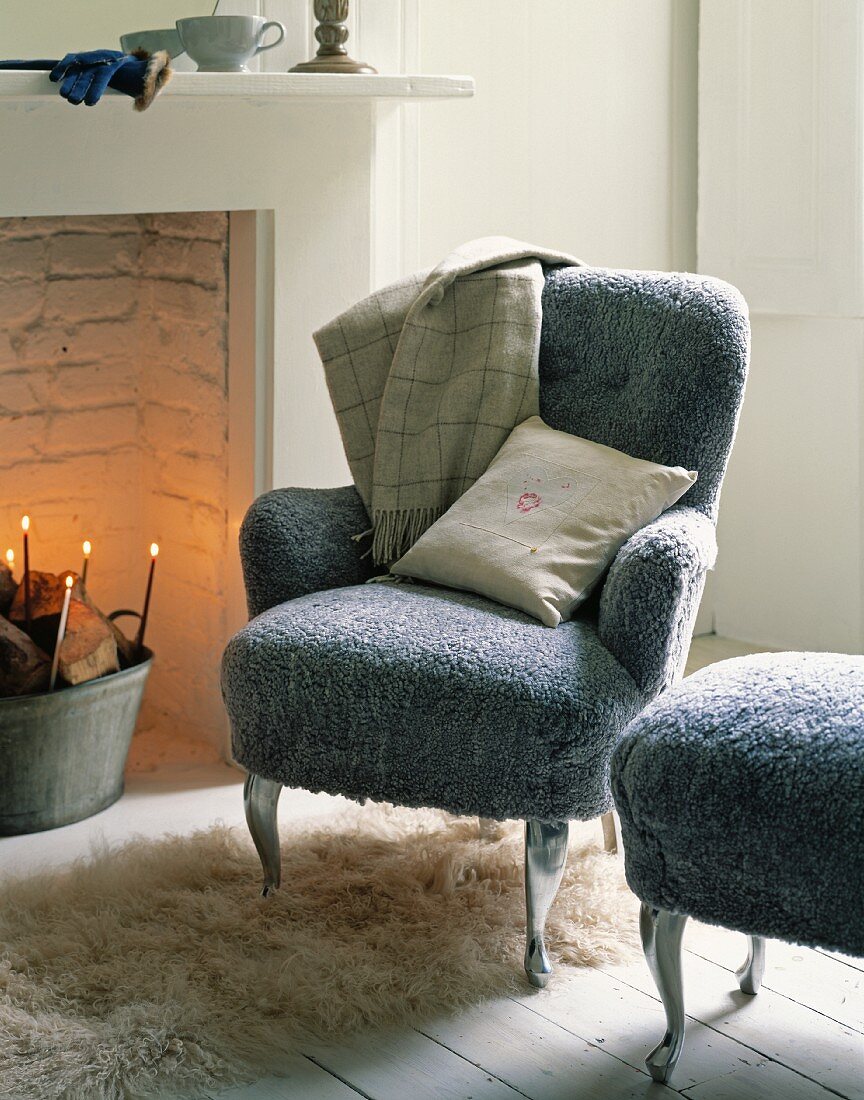 An armchair and a matching stool with fluffy grey covers next to a fireplace in a traditional atmosphere