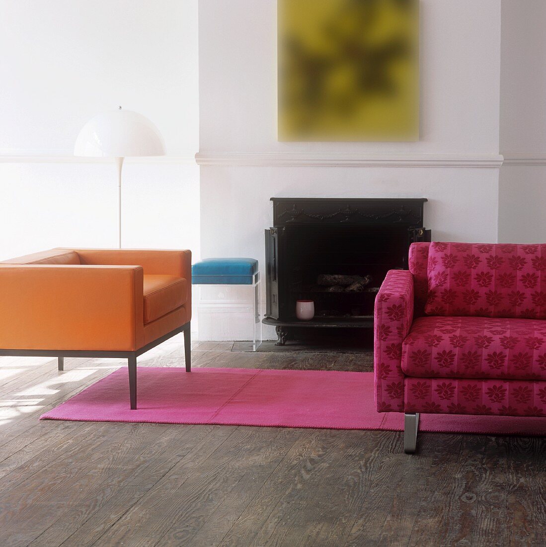 An orange cubic armchair and a pink patterned sofa in front of a fireplace in a traditional atmosphere