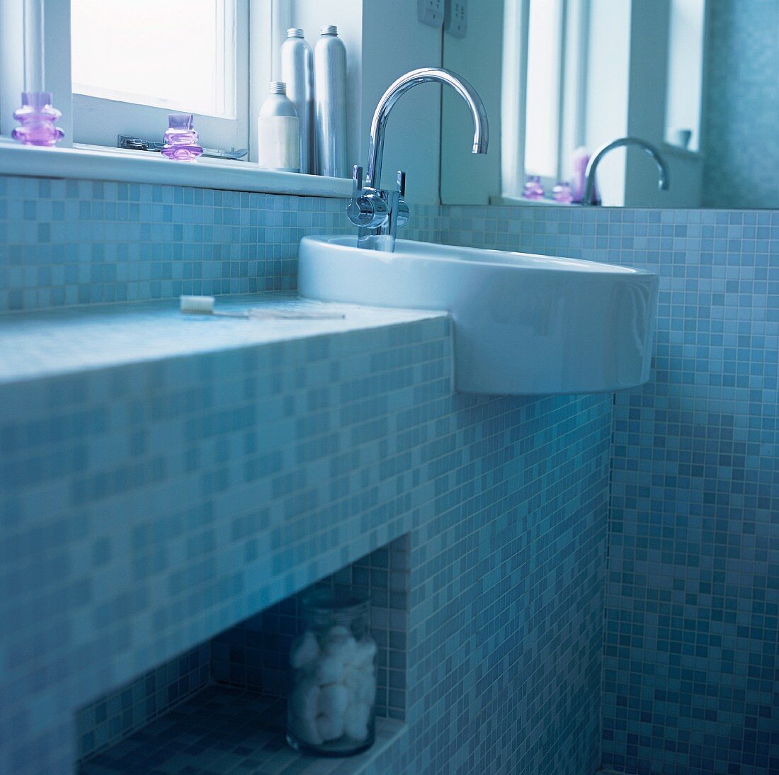 A wash basin under a window in a bathroom decorated with mosaic tiles