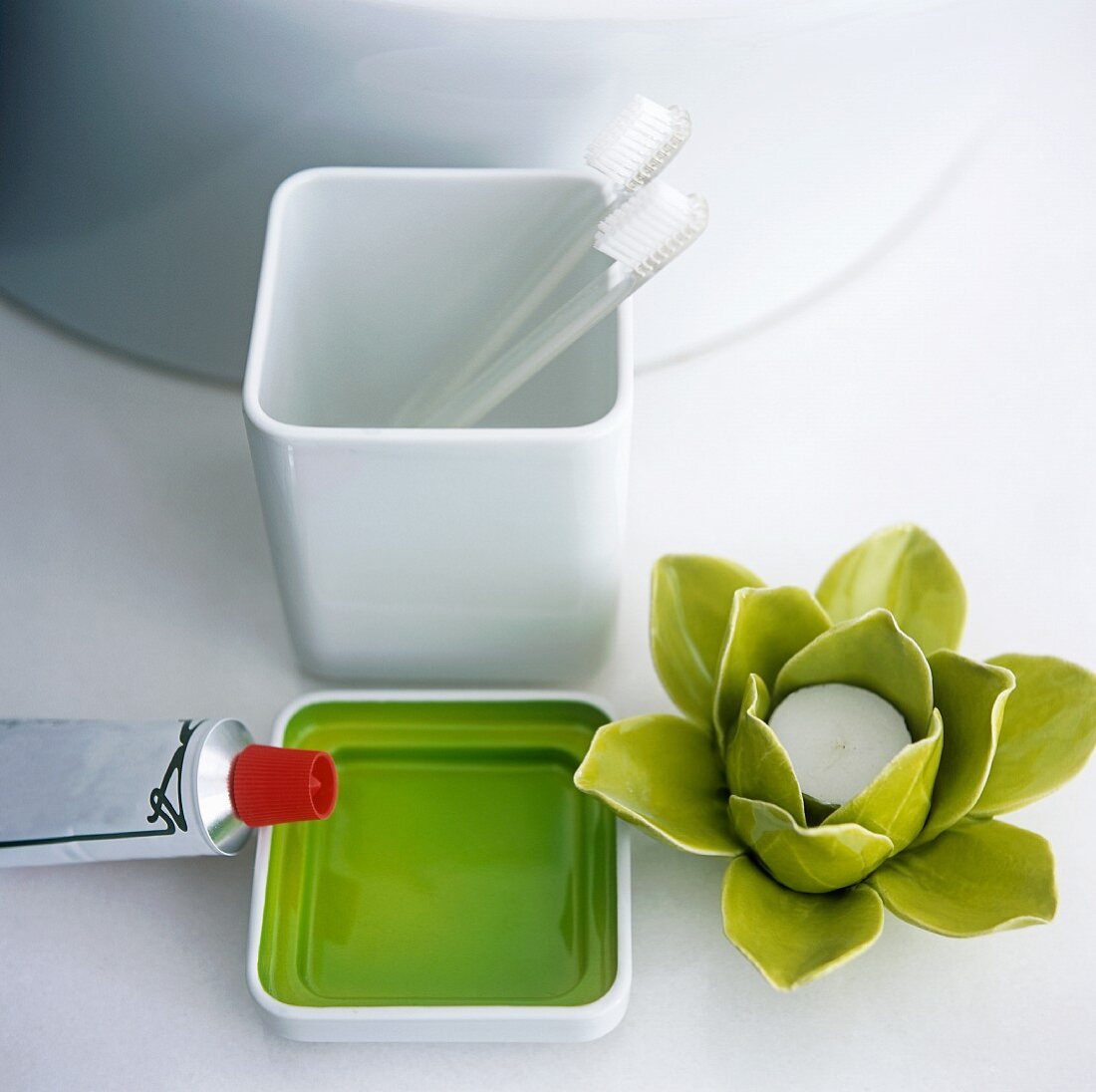 A lilly-shaped candle holder, a bowl, toothpaste and a toothbrushes in a tooth mug