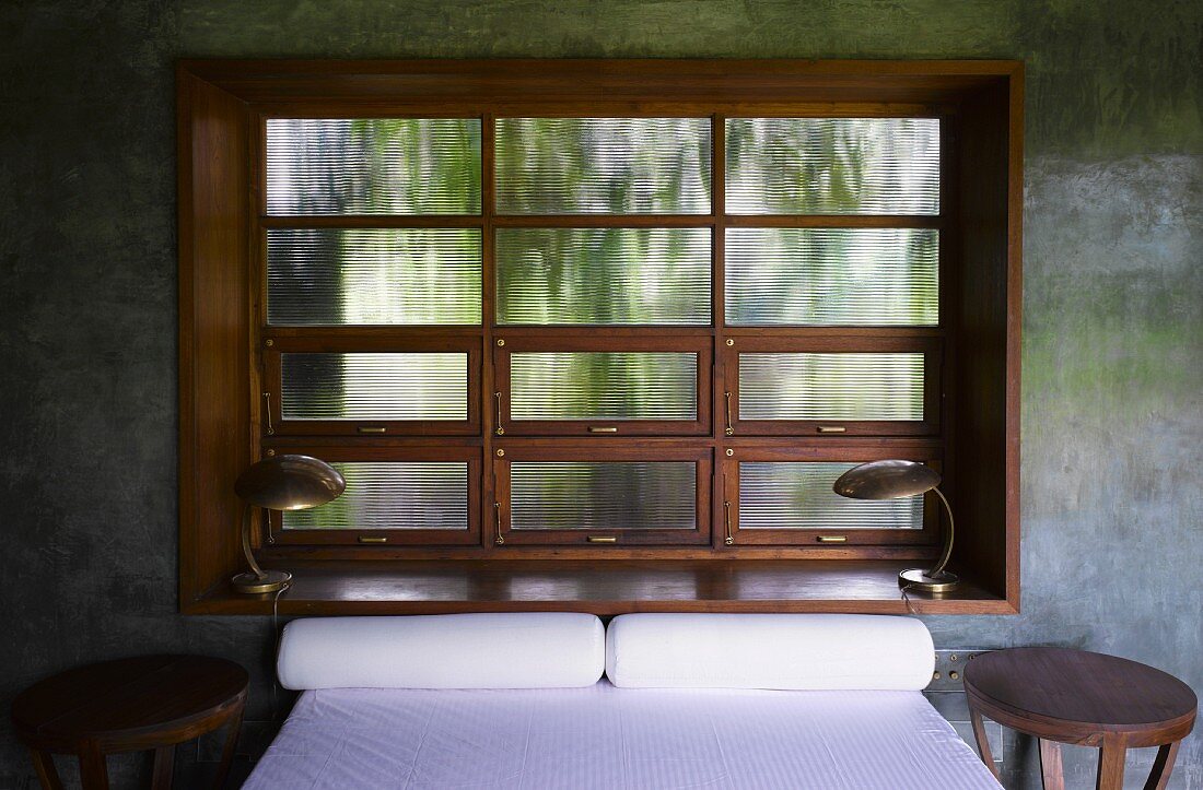 Doppelbett vor traditionellem Sprossenfenster in Betonwand