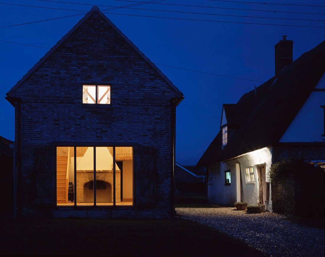 A renovated house by night with illuminated windows and a view of a fireplace