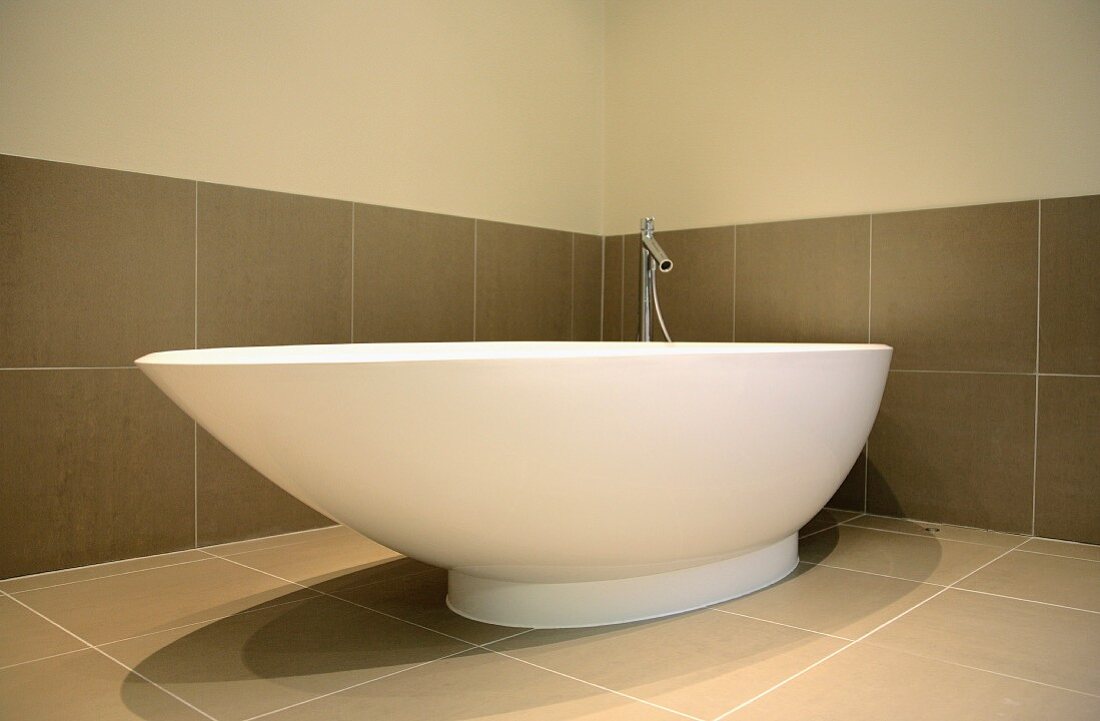 Free-standing, asymmetric bathtub against large tiles in warm grey