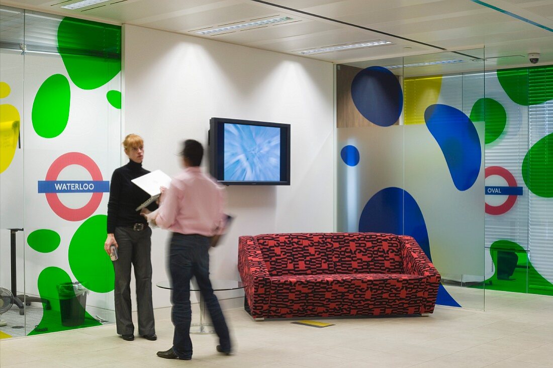 Man and woman in conversation next to wall-mounted flat-screen TV and patterned sofa in front of coloured bubble motifs on partition walls