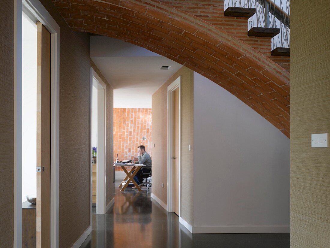 Vaulted brick stairs with wooden treads above a corridor leading to an office with a brick wall