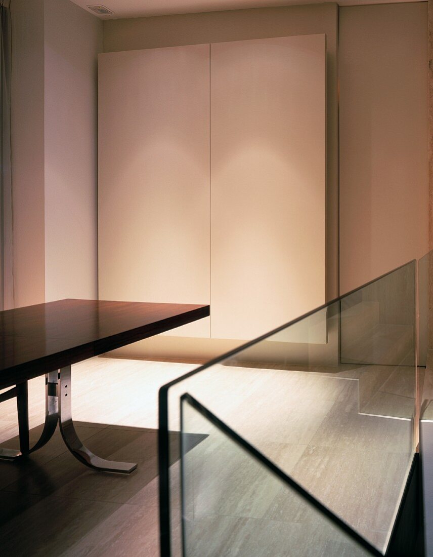 Glass balustrade of staircase and designer dining table in front of made-to-measure cupboard