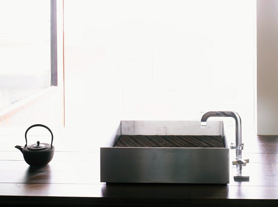 Modern, stainless steel kitchen sink and Japanese teapot on wooden worktop