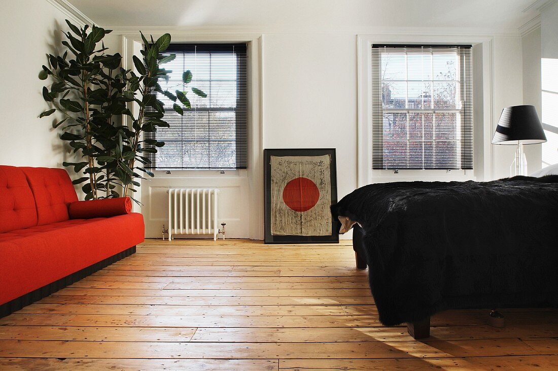 Orange sofa and bed with black bedspread on rustic floorboards