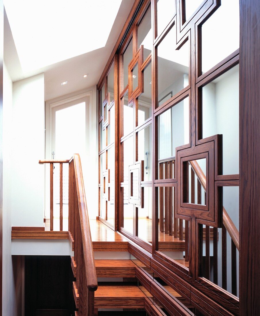 Mirrored wall with elaborate framing beside narrow wooden stairs and an open hall