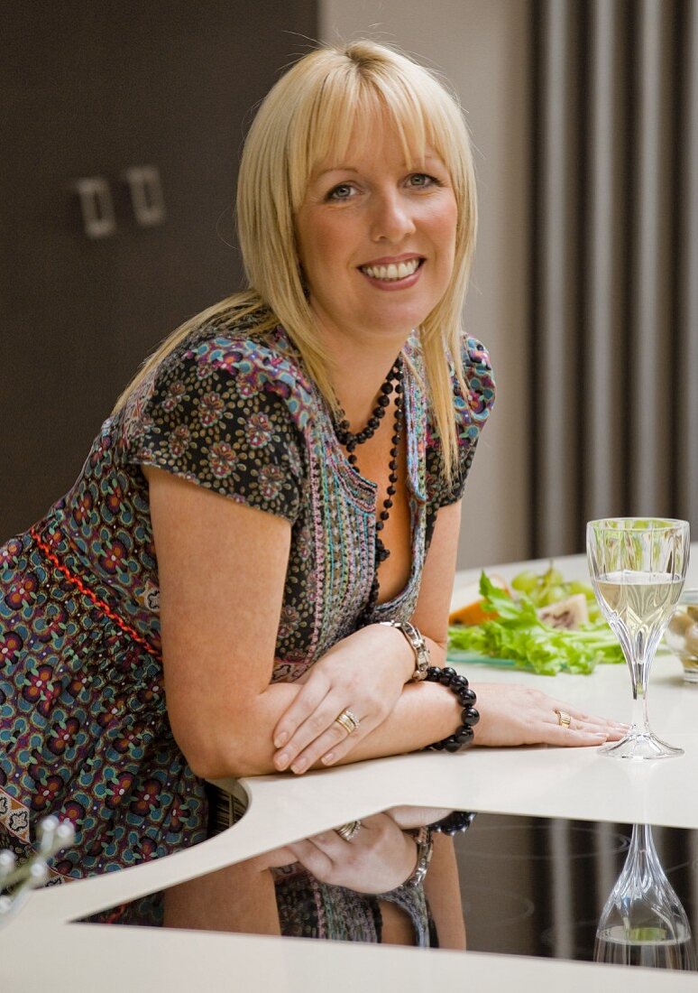 Woman with aperitif leaning on kitchen unit