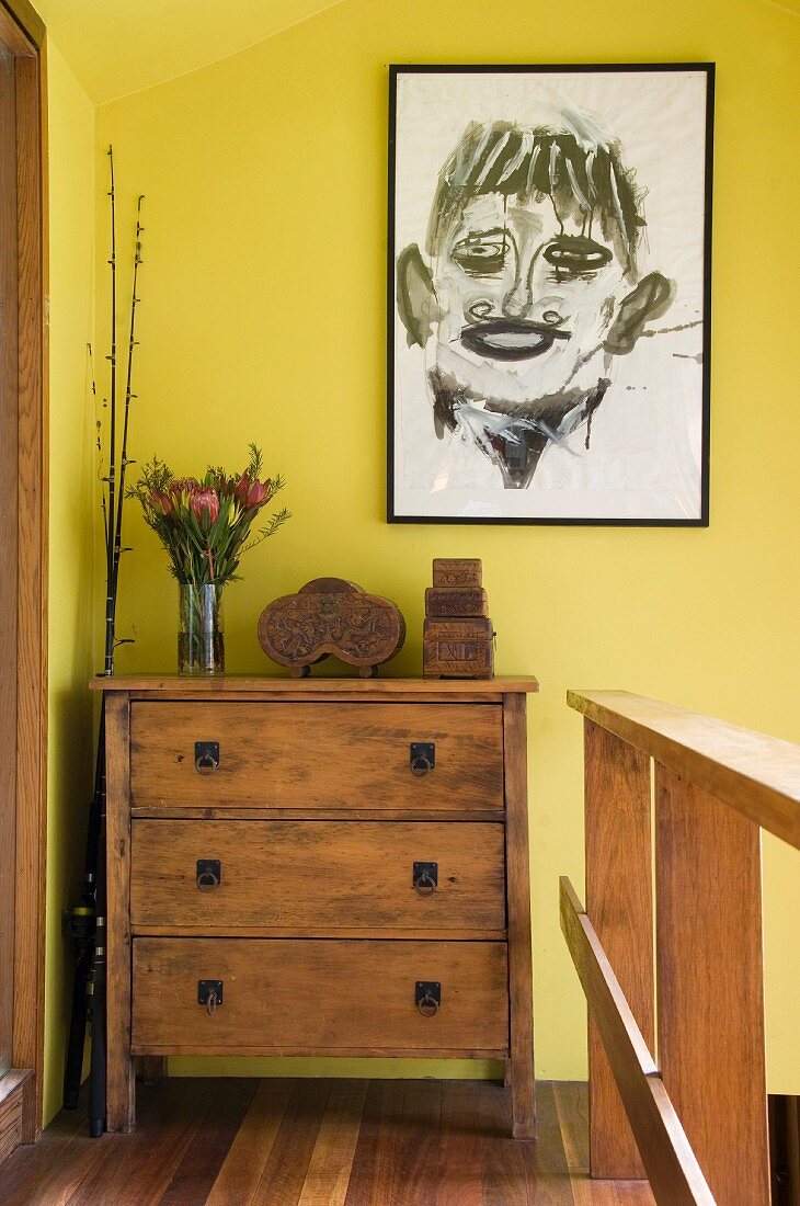 Abstract portrait hanging on a yellow wall above chest of drawers