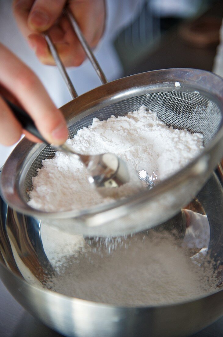 Flour being sieved into a metal bowl