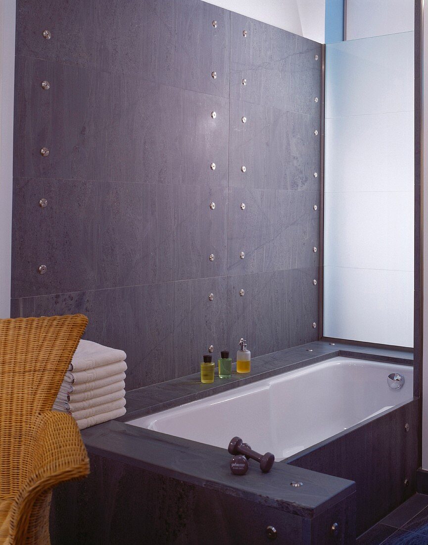 Designer cladding in grey stone on walls and bathtub with stainless steel bolts