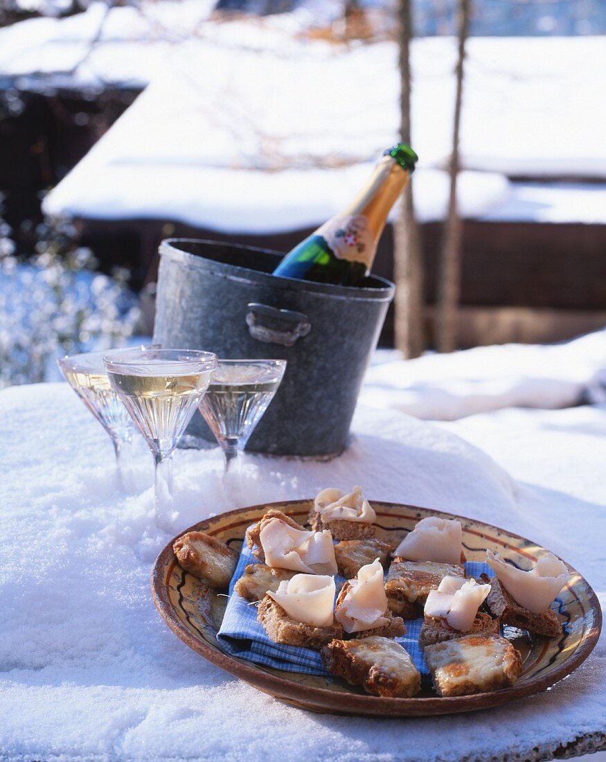 Champagne and a plate of ham canapés in the snow (Chamonix, France)