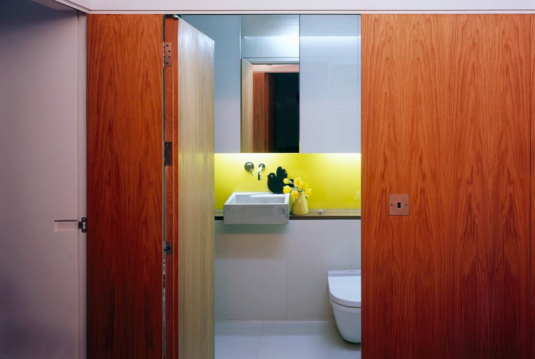 View through open door into small designer bathroom with sink and yellow painted back wall