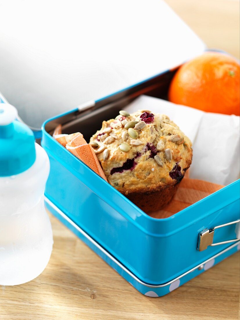 A cranberry muffin and an orange in a lunch box