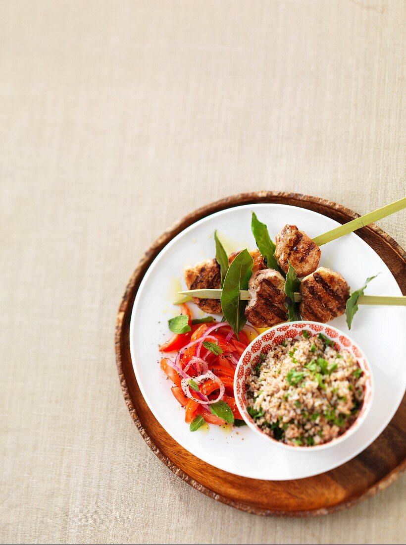 A pork kebab with a tomato salad and bulgur wheat