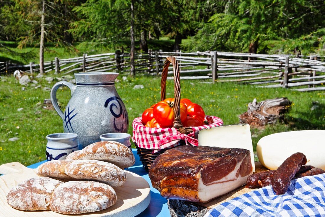 A picnic and alpine meadow with bread, bacon, cheese, sausages, tomatoes and wine