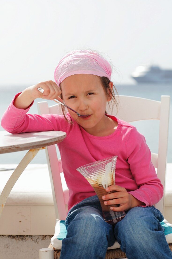 Kleines Mädchen isst Schokoladeneisbecher am Strand