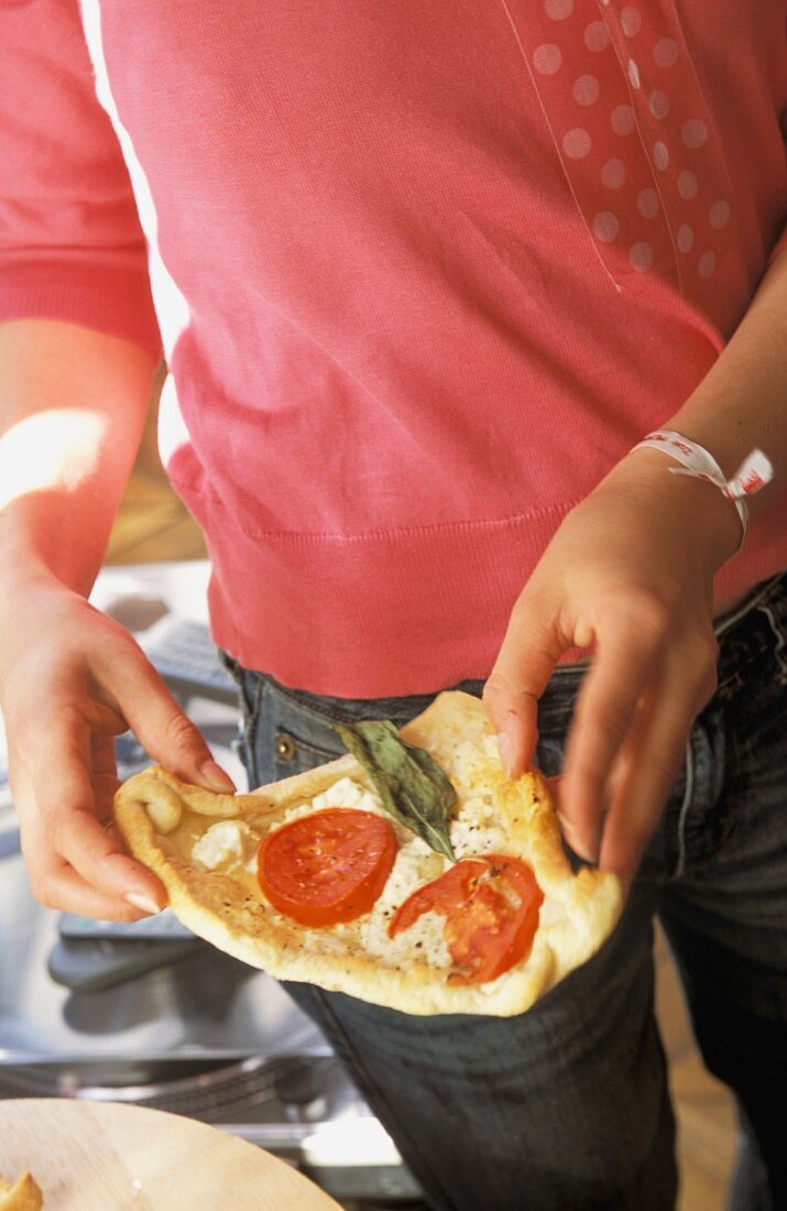 A person holding a slice of tomato pizza