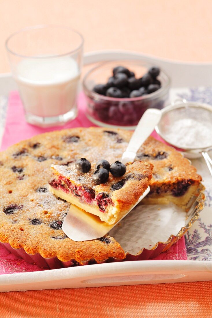 An almond tart with blueberries and icing sugar, sliced