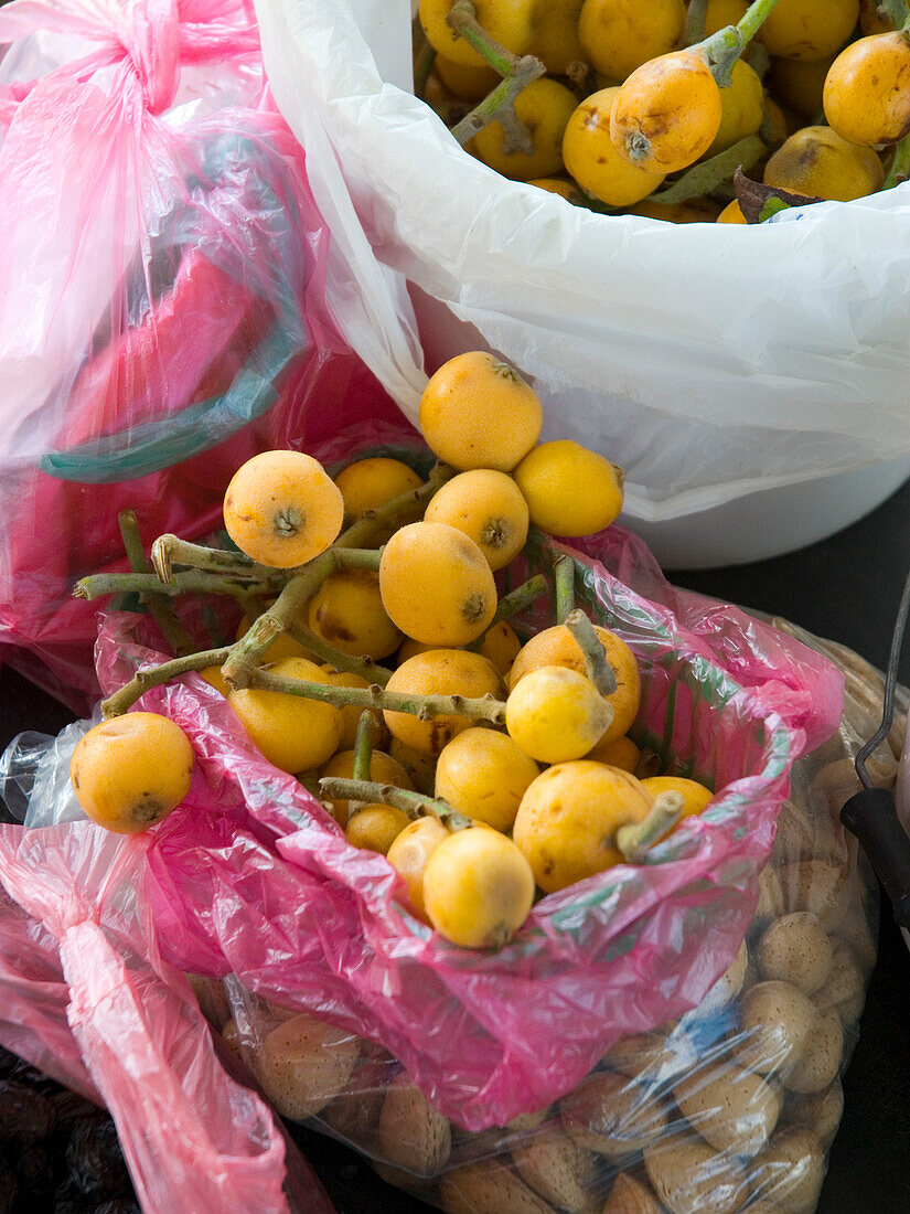 Frische Nisperos (Eriobotrya japonica) in rosafarbenen Plastiktüten auf Marktstand