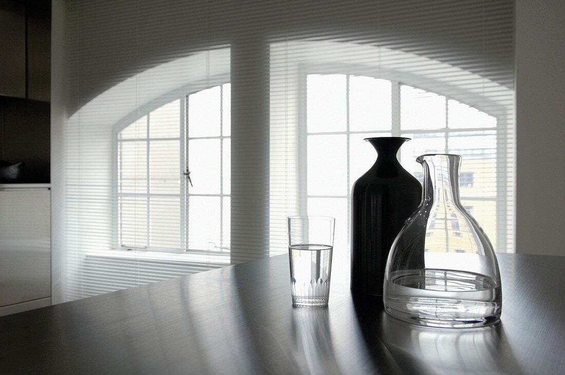 Offene Jalousie vor geteilter Fensterfront mit Segmentbogen, Karaffen und Wasserglas im Vordergrund