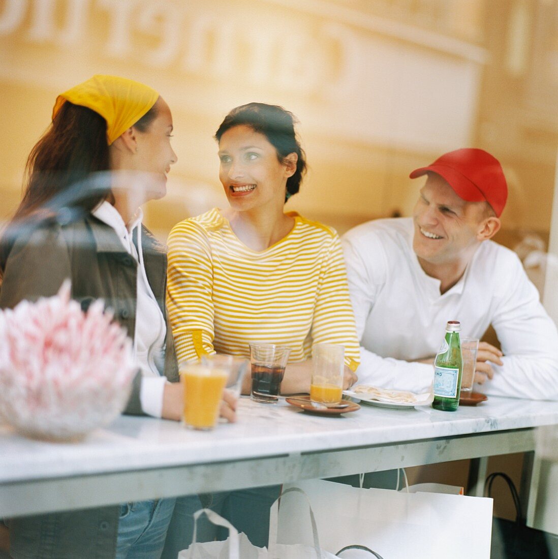 Zwei Frauen und ein Mann mit Getränken in einem Café