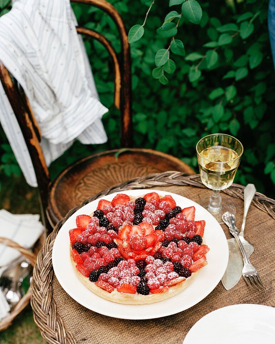 Berry cake and a glass of wine on a garden table
