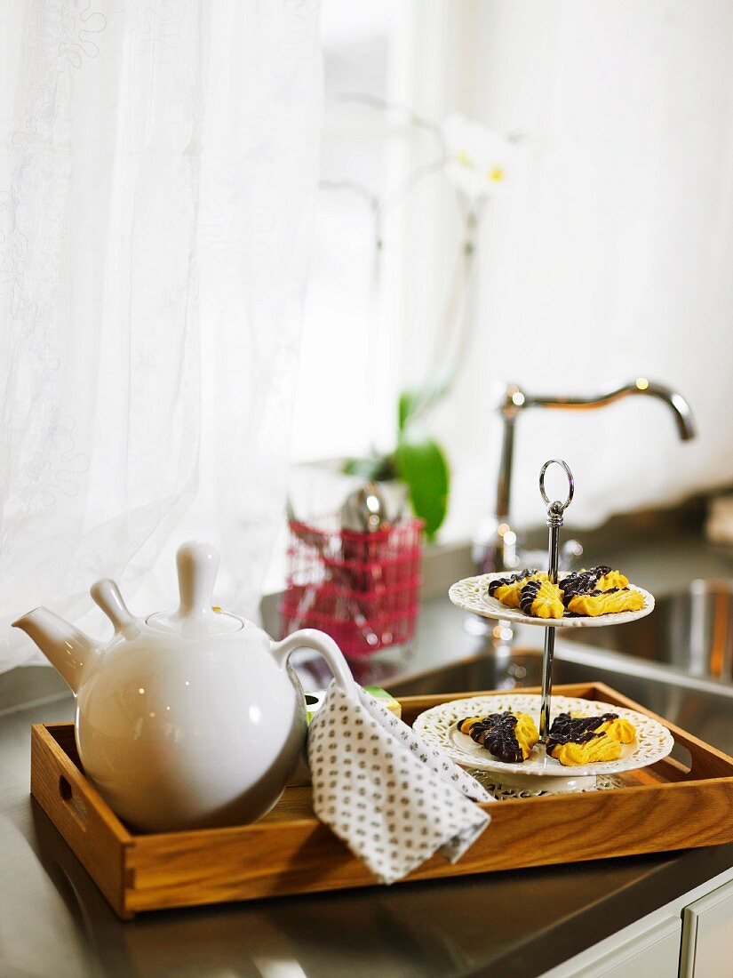 A teapot and biscuits on a wooden tray in a kitchen