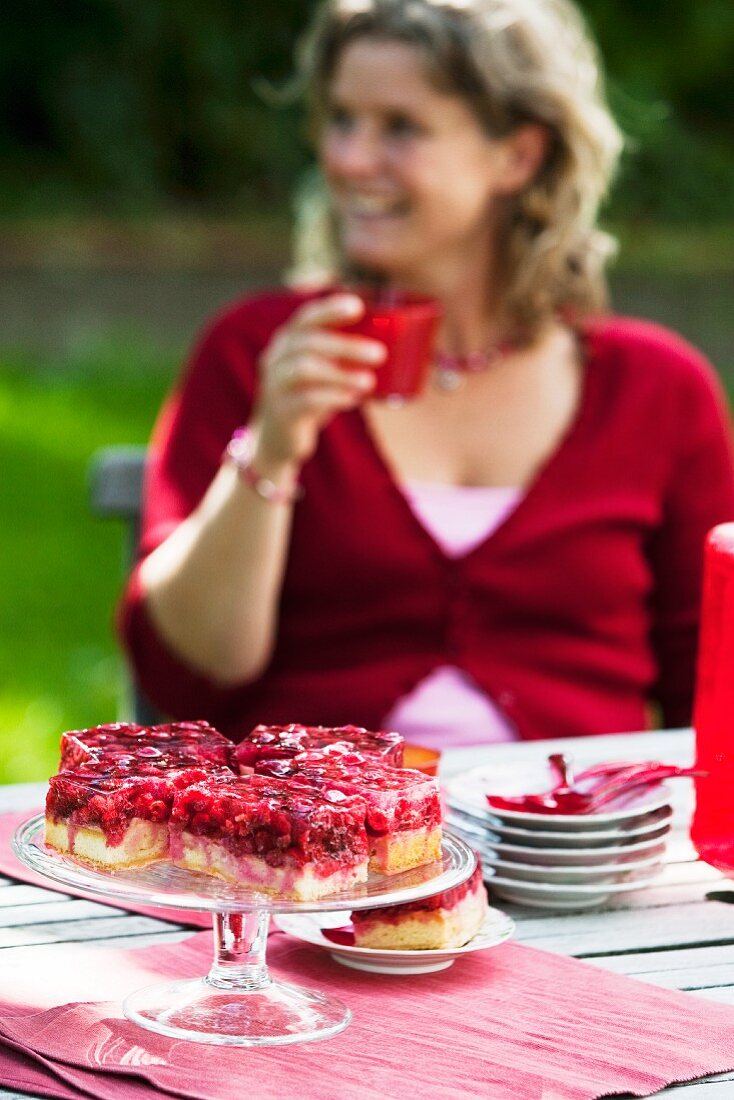 Frau sitzt beim Gartentisch mit Kuchen