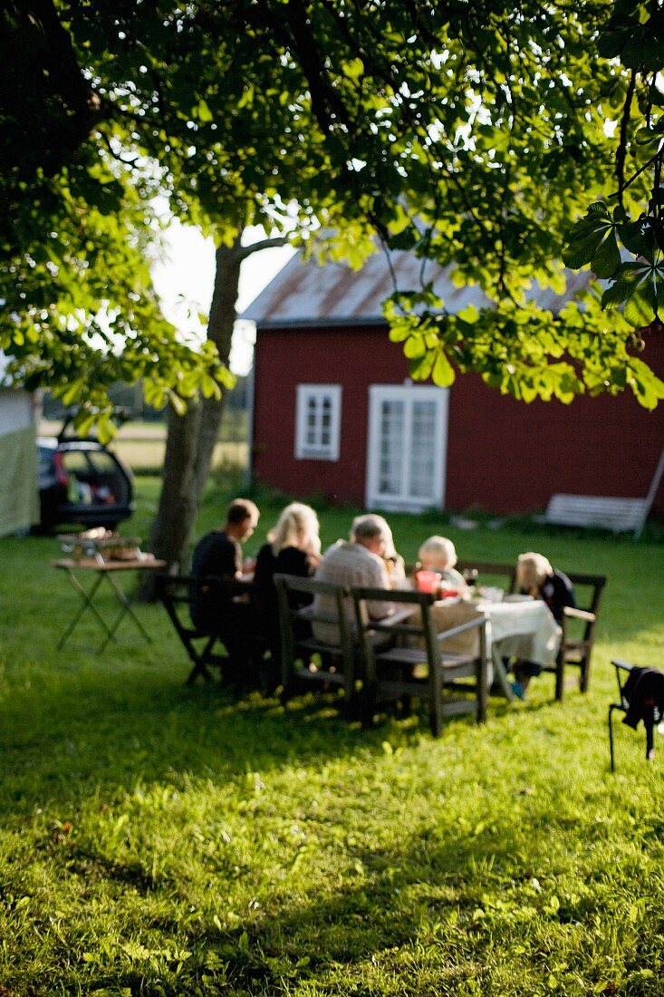 Idyllisches Holzhaus am See mit im Garten essender Familie (Schweden)