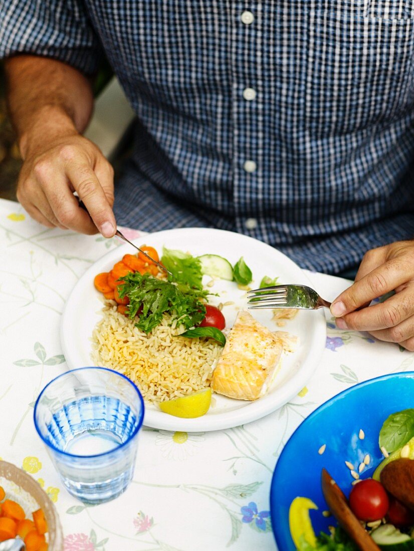 Mann isst Fischfilet mit Reis und Salat