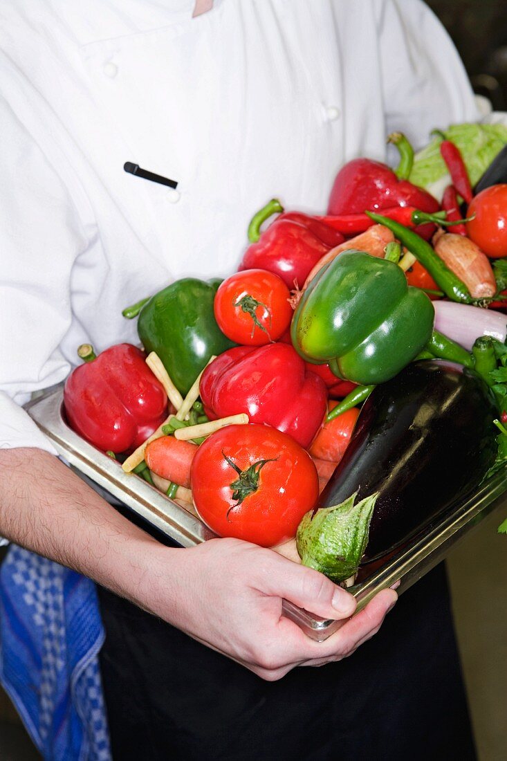 A chef holding a tray of fresh vegetables