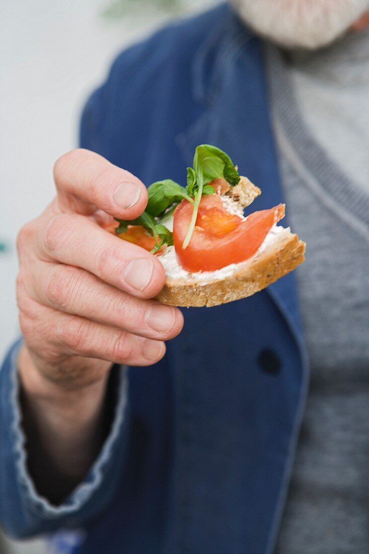 A man holding a slice of bread topped with tomatoes and basil