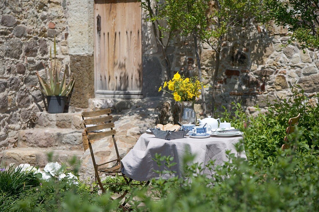 Breakfast table in garden set with yellow flowers in front of Mediterranean stone house