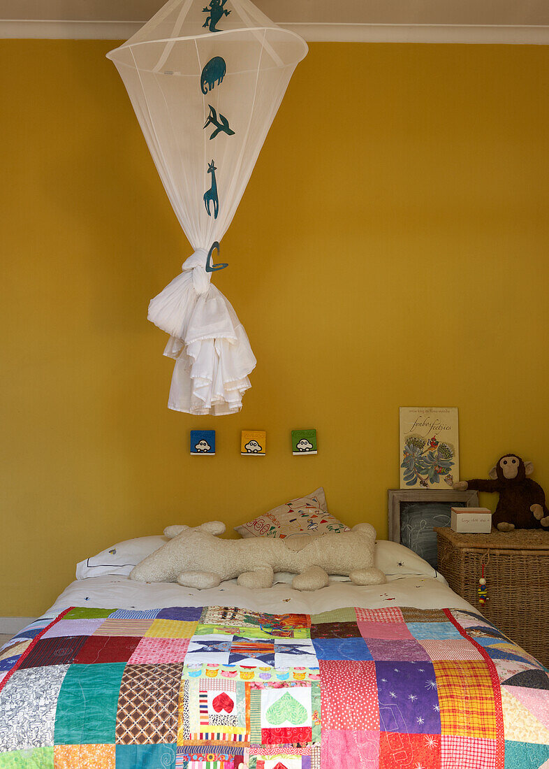 Bed with patchwork quilt and yellow wall in children's room