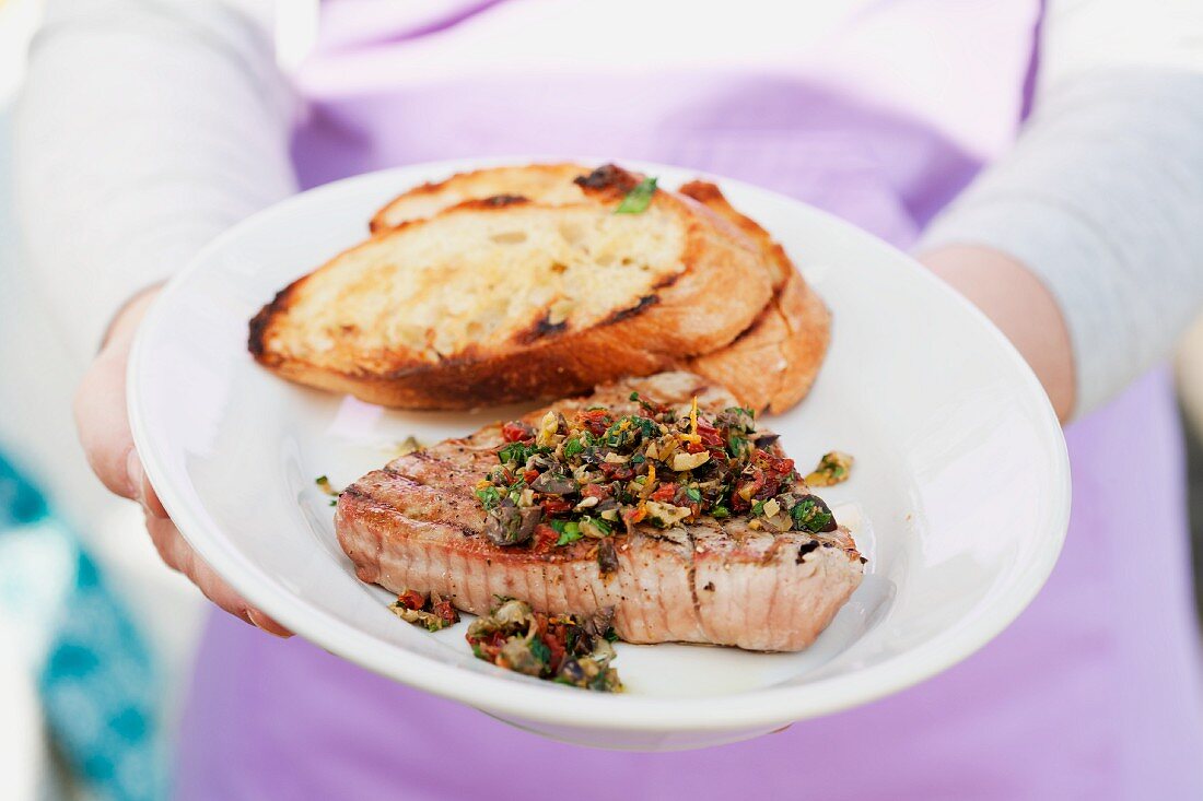 A person holding a plate of steak and bread