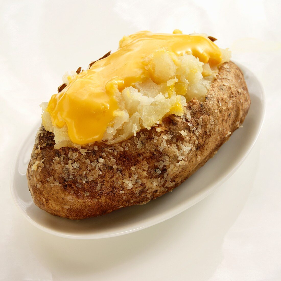 Baked Potato with Salt and Melted Cheese; On a White Plate on a White Background