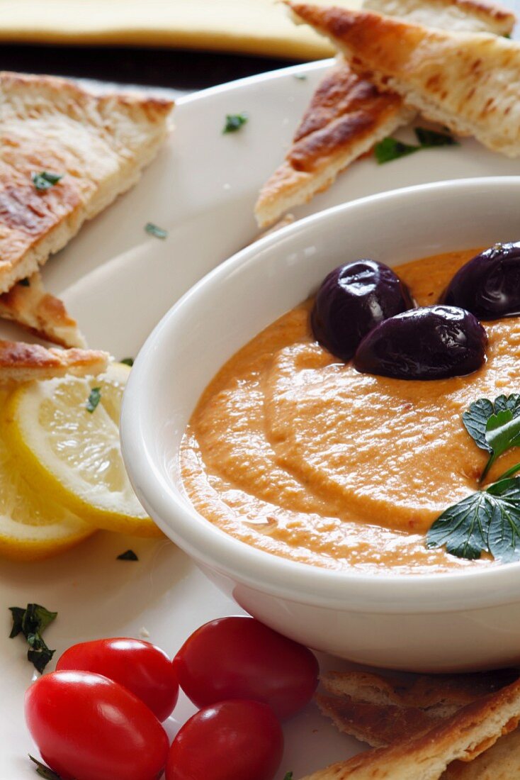 A Bowl of Hummus with Olives, Tomatoes and Toasted Pita Bread Triangles
