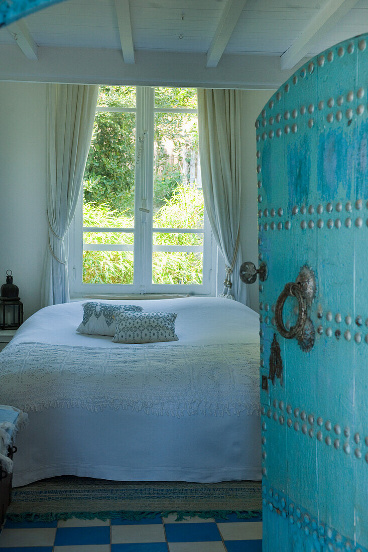 Bedroom with white bed linen, chequered floor, turquoise oriental-style door