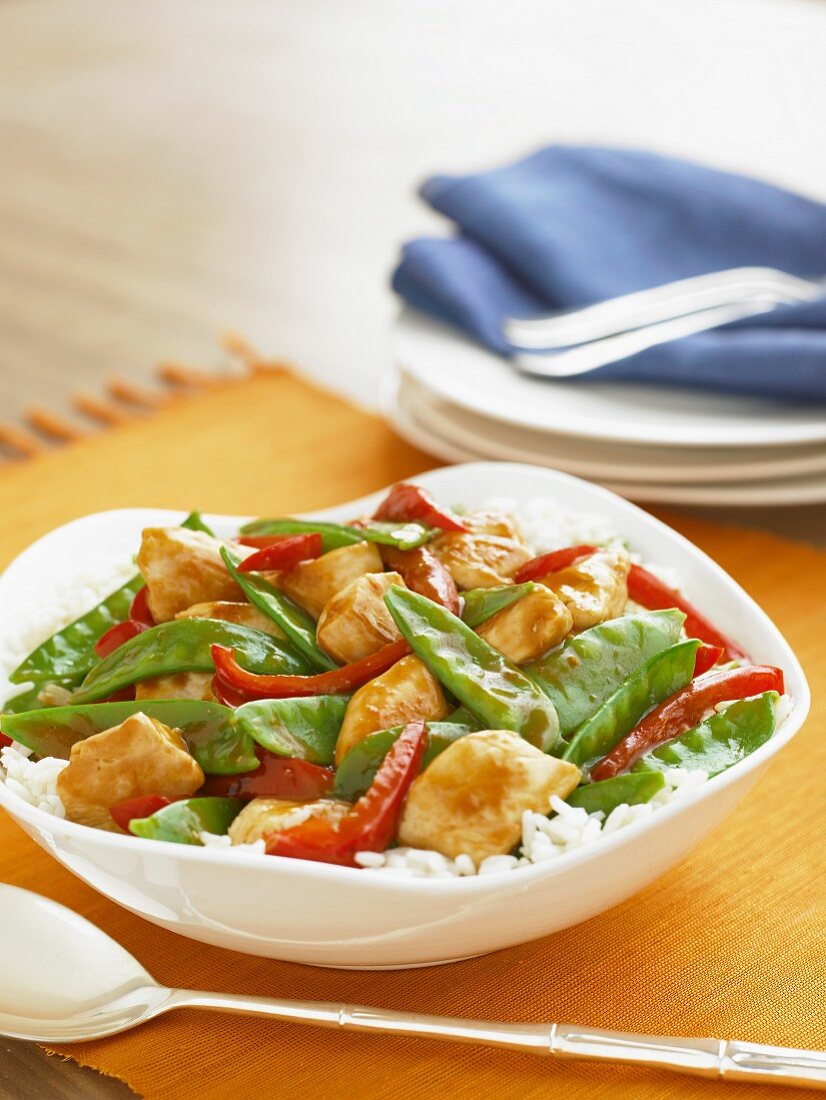Chicken Stir Fry with Snow Peas and Red Peppers Over Rice in a Serving Bowl