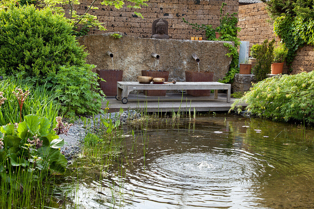 Gartenteich mit Pflanzen und rustikaler Wandbrunnen aus Stein