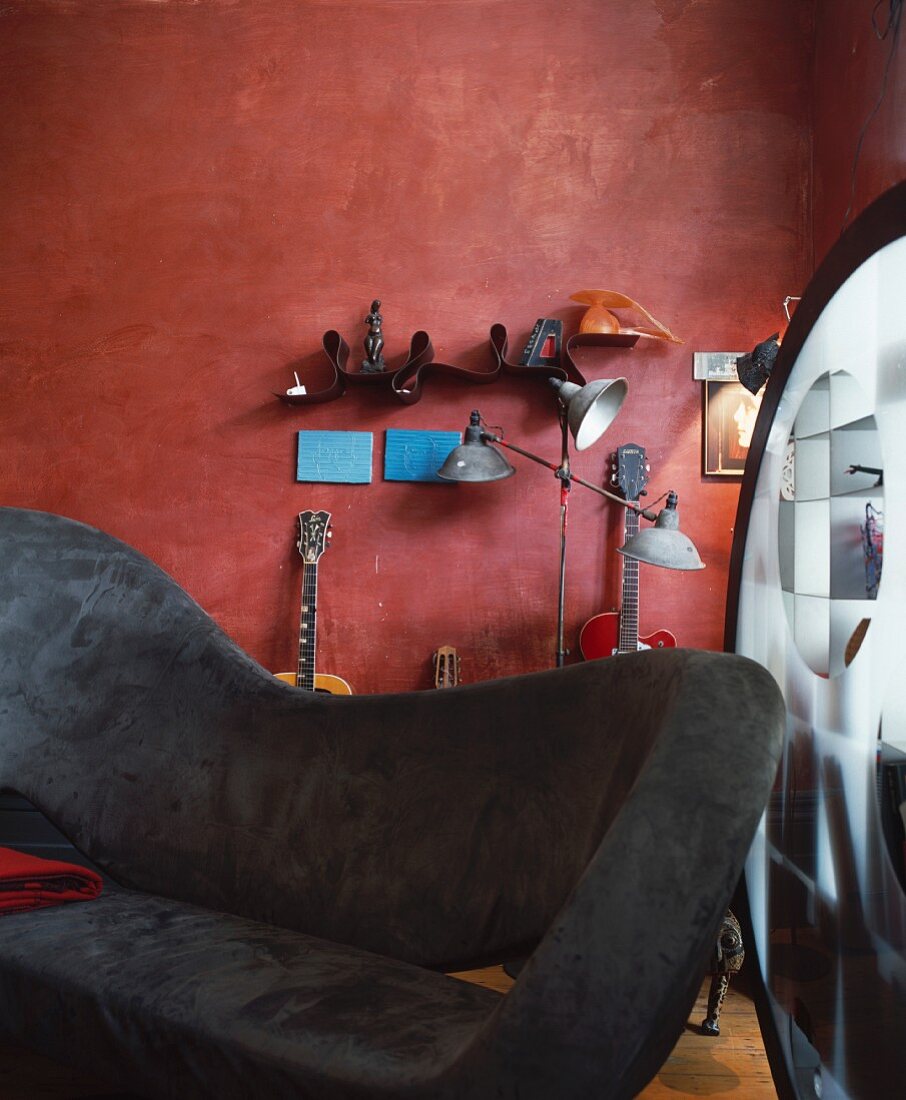 Modern sofa with grey velvet upholstery in front of musical instruments leaning against a rust-coloured wall