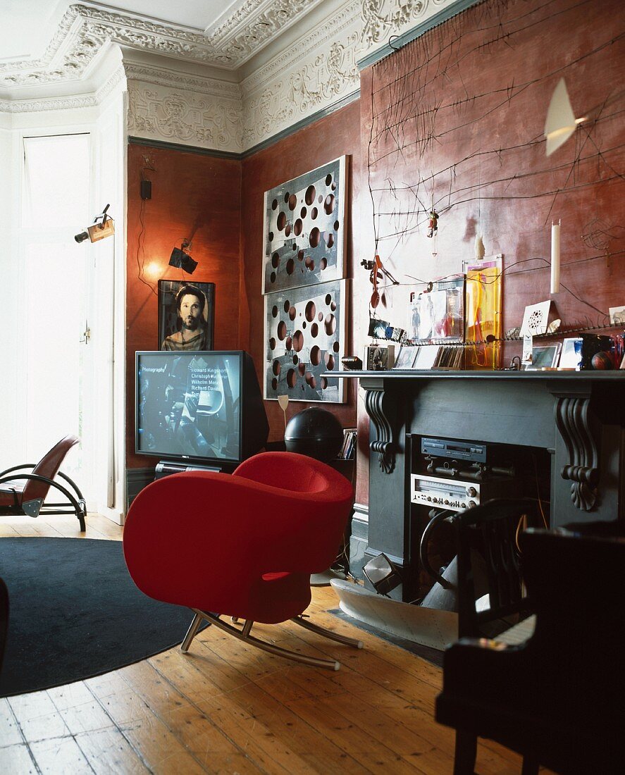 Red designer armchair in front of fireplace containing stereo in luxurious Baroque-style living room