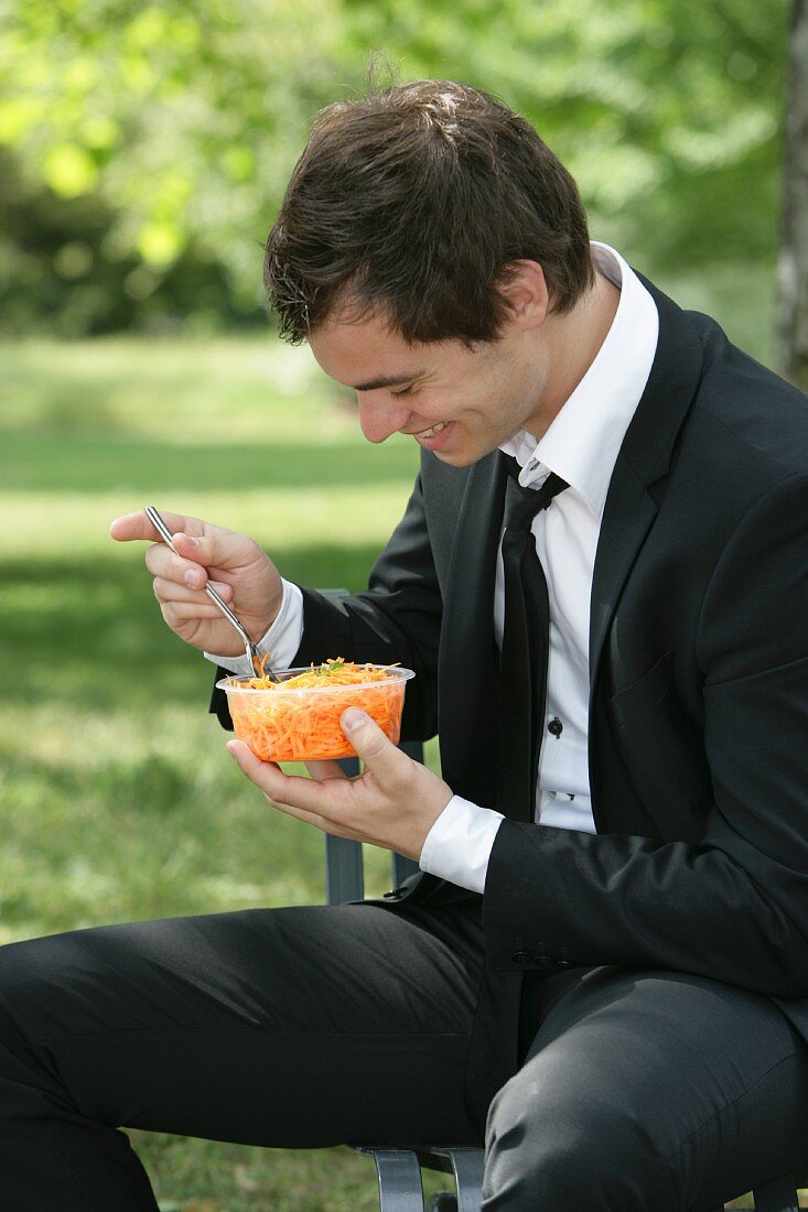 A man eating grated carrots on a park bench