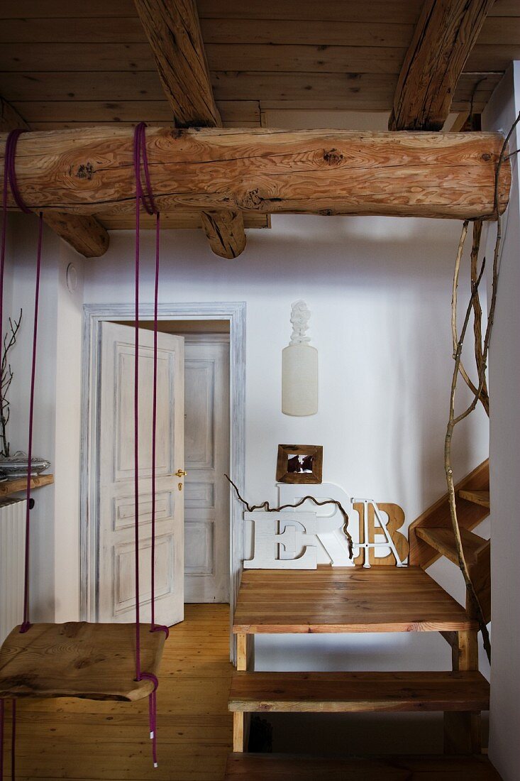 Swing suspended from wooden beam below ceiling and wooden staircase with landing